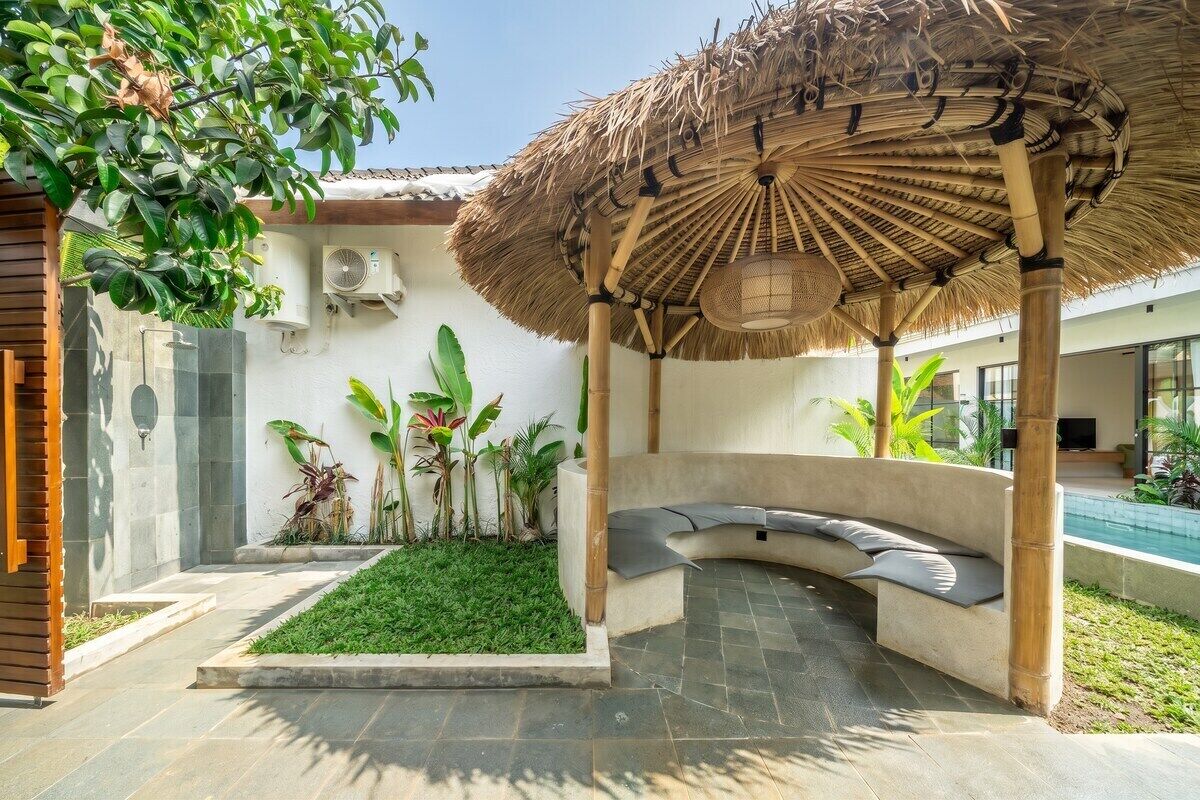 A covered outdoor seating area with a pool in the background.