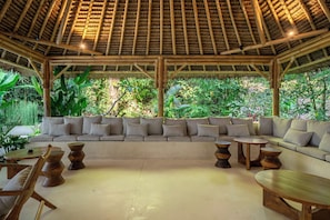 A covered outdoor seating area with a thatched roof, surrounded by lush greenery. - Designer 3BR Villa in Ubud w Pool, Patio & Garden (Gianyar Regency)