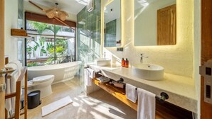 Un baño moderno con bañera, dos lavamanos, un espejo grande y vistas a zonas verdes.