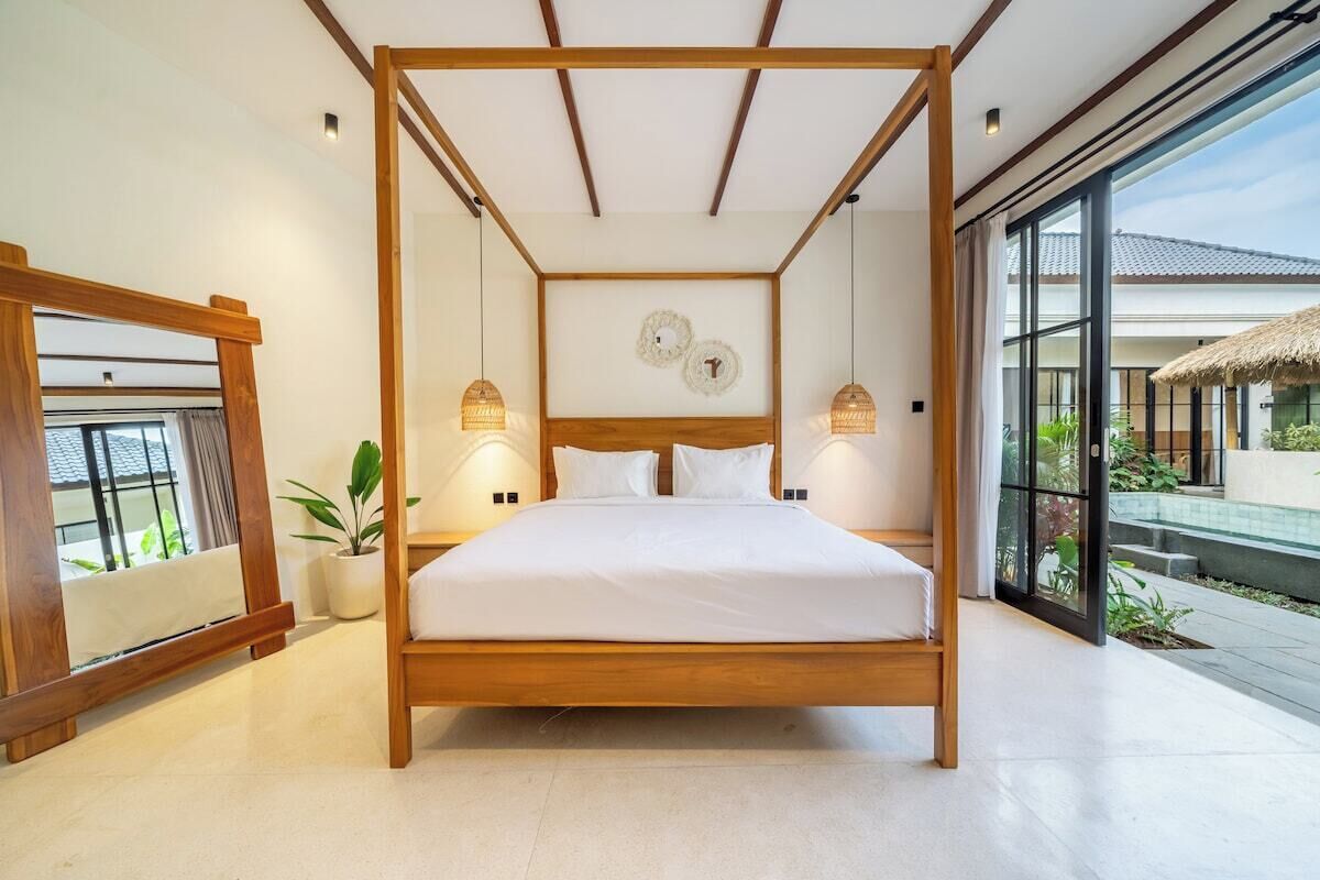 A modern bedroom with a wooden four-poster bed, bedside lamps, and a view of the outside.