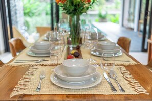 A dining table set with plates, bowls, glasses, and cutlery, with a vase of flowers in the center. - Tropical 3BR Villa in Ubud w Pool, Patio & Garden (Gianyar Regency)