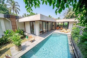 Una casa moderna amb piscina, mobiliari exterior i plantes tropicals.