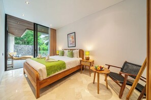 A modern bedroom with a large bed, a bedside table, a chair, and a view of greenery outside. - Tropical 3BR Villa in Ubud w Pool, Patio & Garden (Gianyar Regency)
