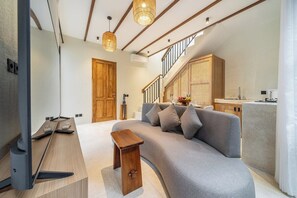 Uma sala de estar moderna com um sofá cinza, mesa lateral de madeira e uma TV sobre um suporte de madeira.