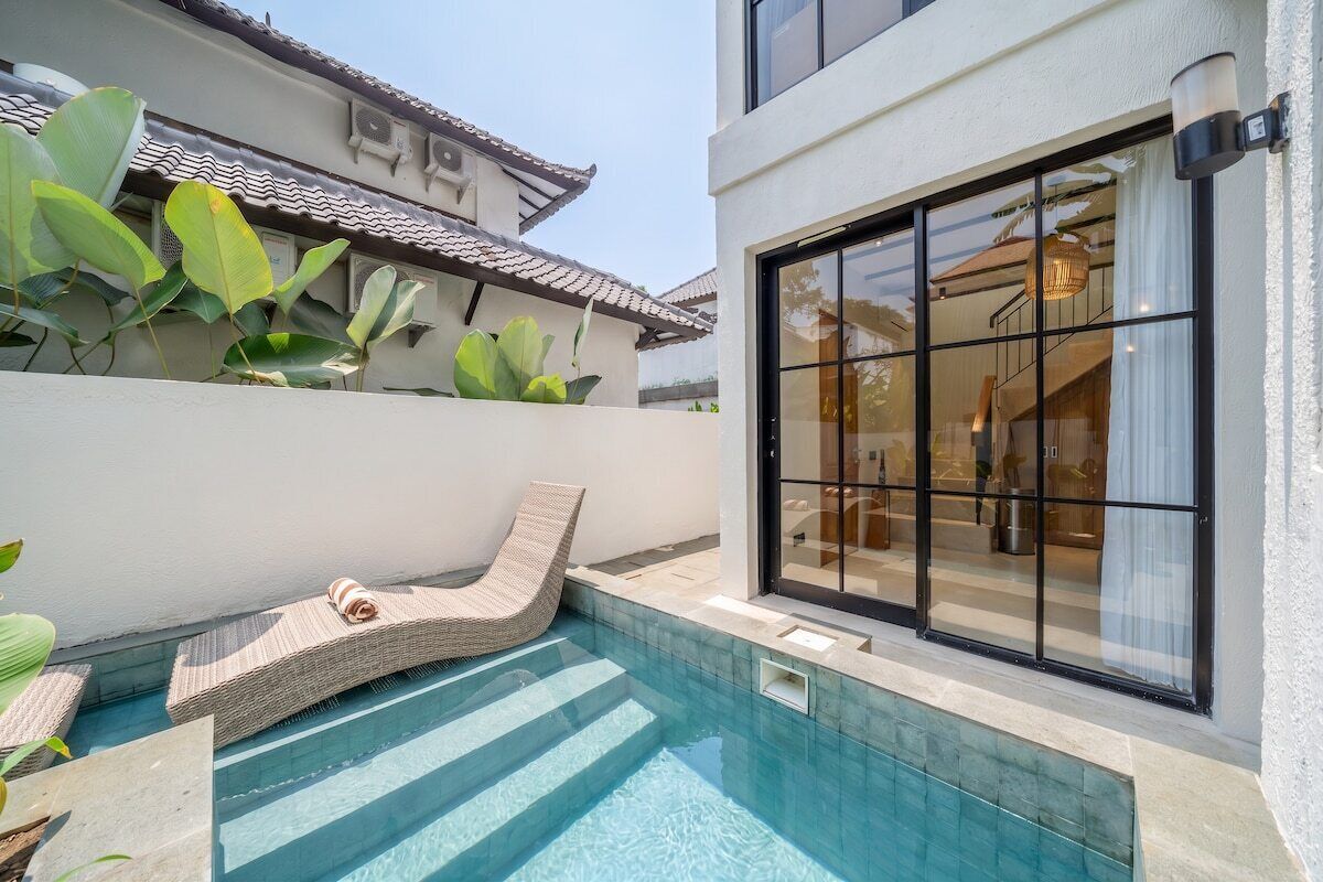 A modern pool area with a lounge chair, a large window, and a tiled roof.