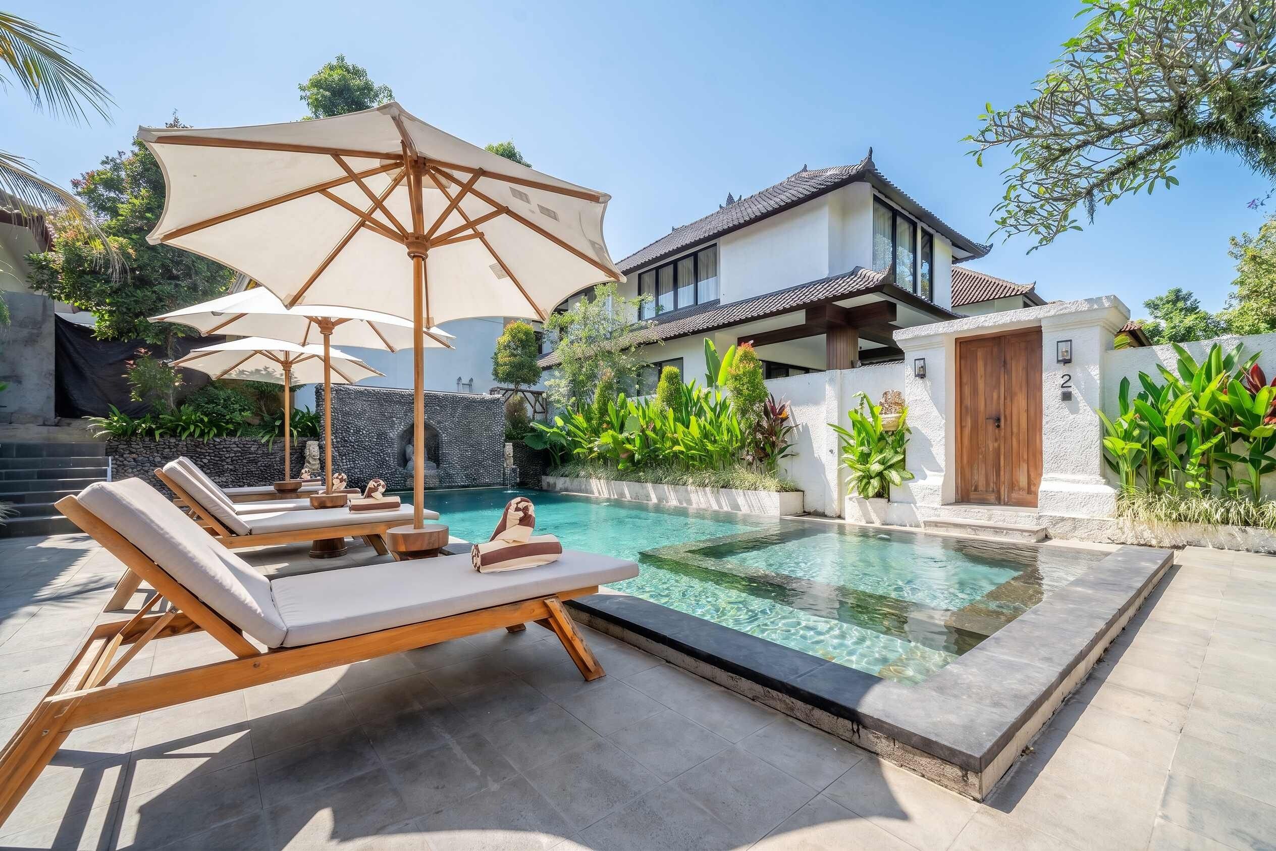 A pool area with lounge chairs and umbrellas, a stone wall, and a traditional building in the background.
