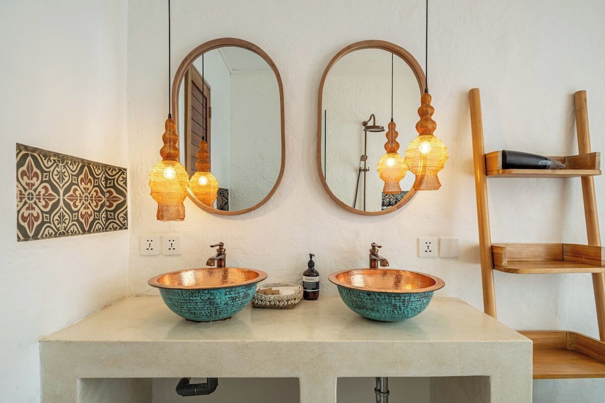 A bathroom with two copper sinks, a wooden shelf, and a mirror with a showerhead.