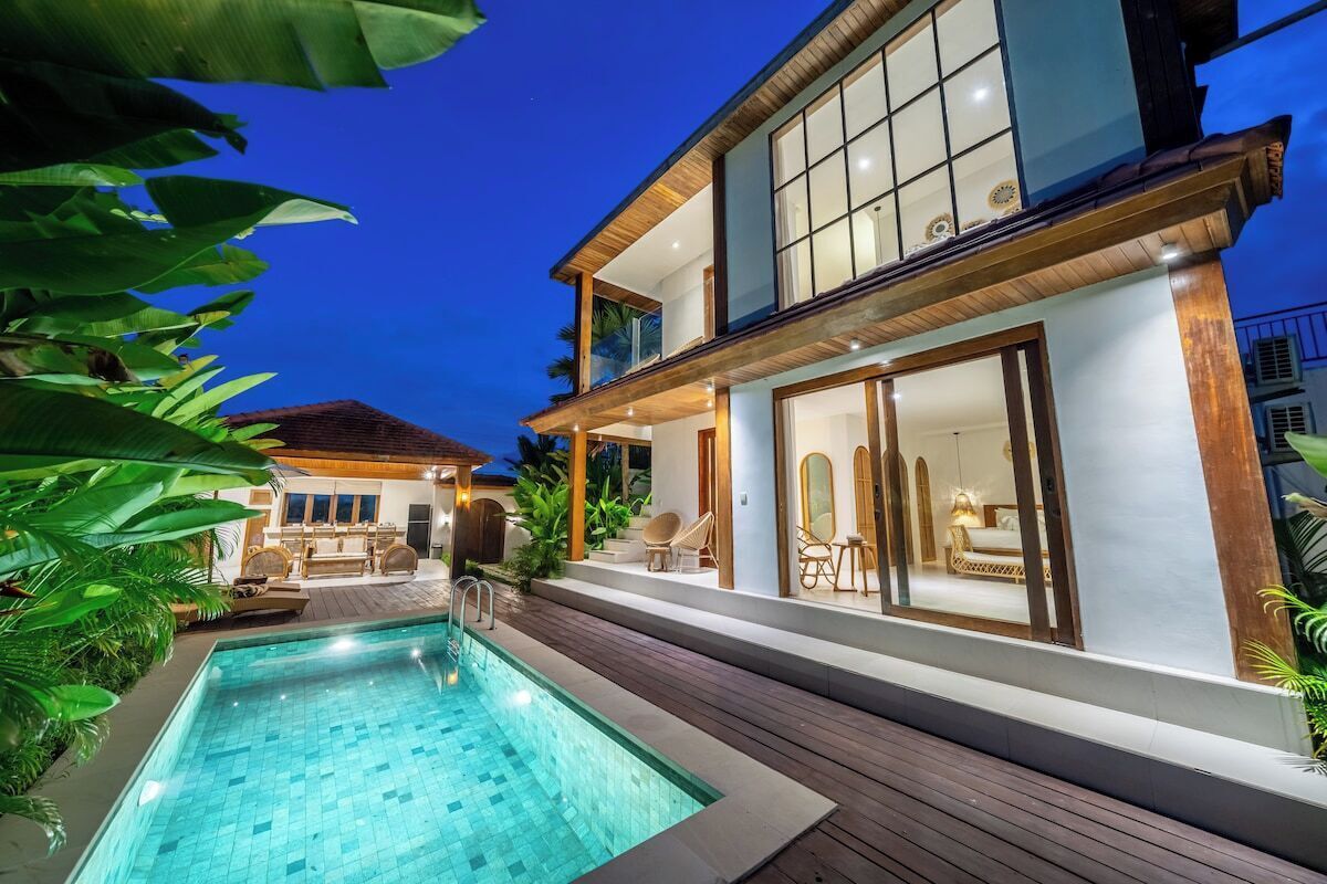 A two-story house with a swimming pool, outdoor seating, and a well-lit interior.