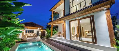 A two-story house with a swimming pool, outdoor seating, and a well-lit interior.