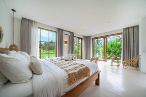 Ein geräumiges Schlafzimmer mit einem großen Bett, Blick auf üppiges Grün und einem Balkon mit Korbmöbeln.