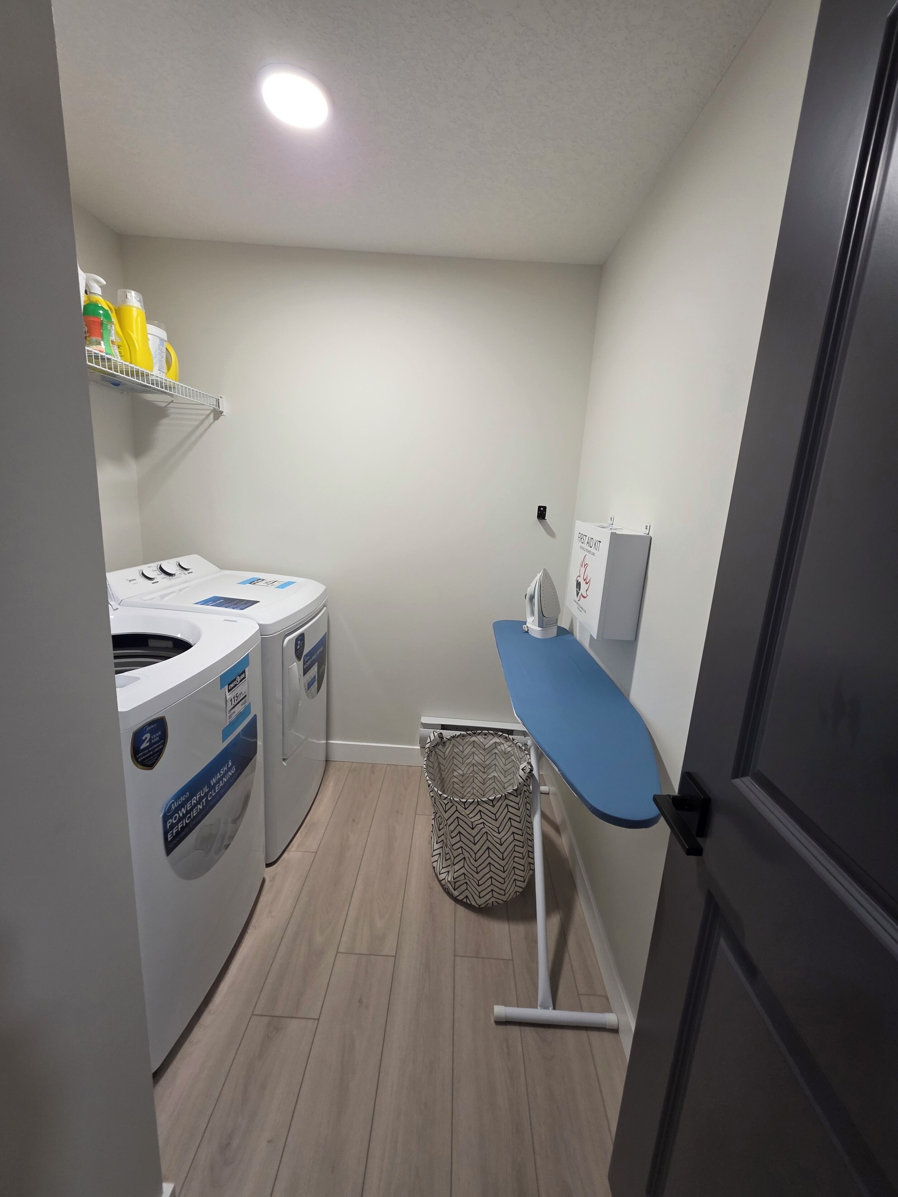 A laundry room with two front-loading washing machines, a drying rack, and a basket.