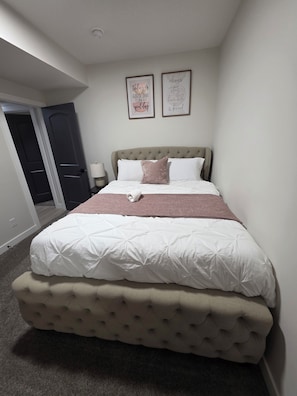 Una camera da letto con un letto grande, una testiera, due poster motivazionali incorniciati, una lampada da comodino e una porta che dà su un'altra stanza.