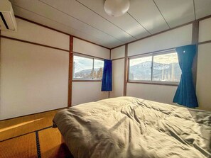 A room with a bed, two windows, and a view of a mountain.
