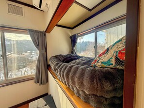 A cozy bed with a view of a snowy landscape, a window with curtains, and a patterned pillow.