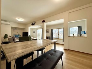 Ein modernes Wohnzimmer mit einem Holzes Esstisch, einer schwarzen gepolsterten Bank und einem großen Fenster mit Vorhängen.