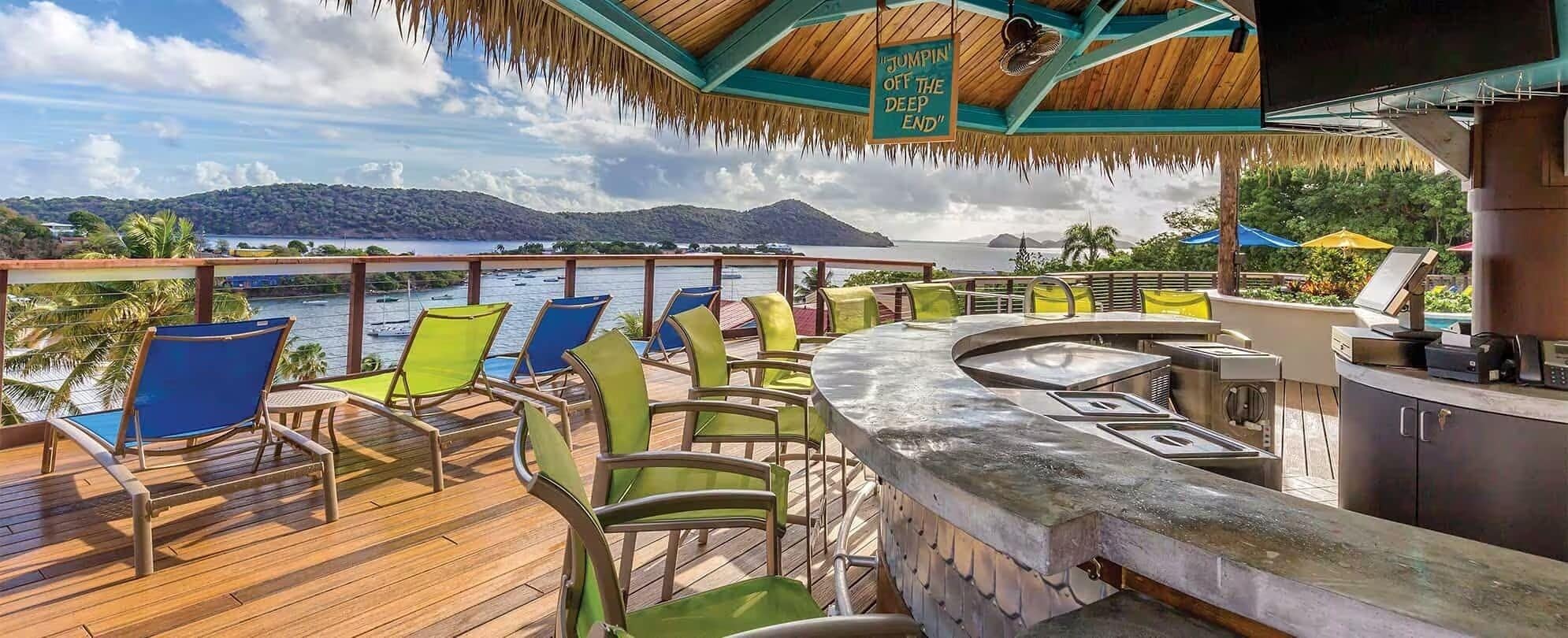 A deck with outdoor seating and a bar area, overlooking a body of water and a mountainous landscape.
