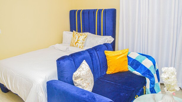 A hotel room with a bed, a blue sofa, and a white curtain. - Alasiri Apartments Utawala (Nairobi)