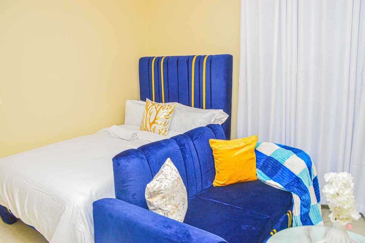 A hotel room with a bed, a blue sofa, and a white curtain.