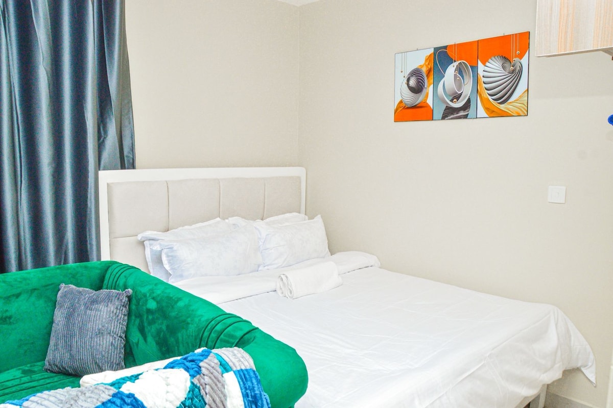 A hotel room with a bed, a green armchair, and a painting on the wall.