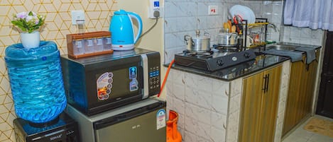 A compact kitchen with a microwave, a water dispenser, a kettle, and a gas stove.