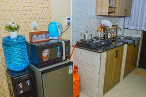 A compact kitchen with a microwave, a water dispenser, a kettle, and a gas stove. - Alasiri Apartments Utawala (Nairobi)