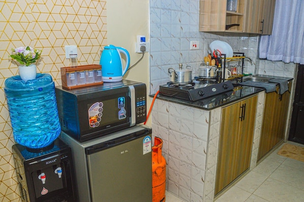 A compact kitchen with a microwave, a water dispenser, a kettle, and a gas stove. - Alasiri Apartments Utawala (Nairobi)