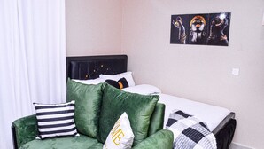 A bedroom with a bed, a green sofa, and a painting on the wall. - Alasiri Apartments Utawala (Nairobi)