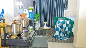 A compact kitchen with a gas stove, pots, a water dispenser, and a small table with a vase. - Alasiri Apartments Utawala (Nairobi)