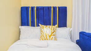 A bed with white bedding and a blue headboard with yellow stripes. - Alasiri Apartments Utawala (Nairobi)