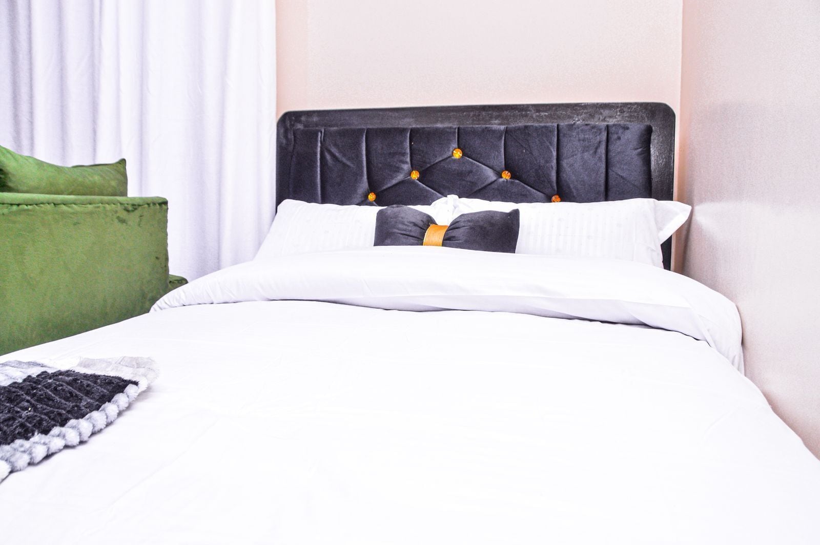 Una cama con cabecera capitonada, ropa de cama blanca y una almohada verde.
