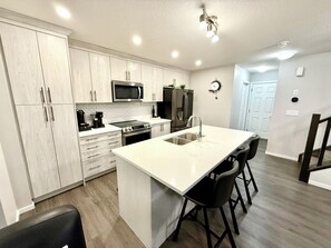 A modern kitchen with a central island, stainless steel appliances, and a white backsplash. - Free Car garage|3BR|YYC|Banff|Canmore|Winsport|Stampede (Calgary)