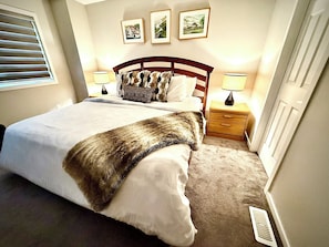 A bedroom with a large bed, two bedside tables with lamps, a carpeted floor, and a window with blinds. - Free Car garage|3BR|YYC|Banff|Canmore|Winsport|Stampede (Calgary)