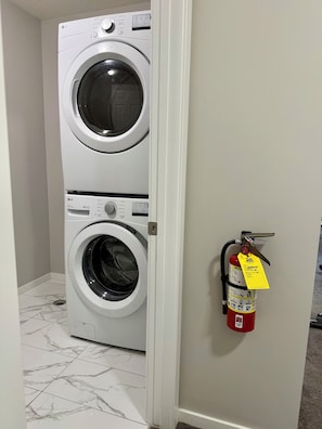 A laundry room with a stacked washer and dryer, a fire extinguisher on the wall, and a tiled floor. - Free Car garage|3BR|YYC|Banff|Canmore|Winsport|Stampede (Calgary)