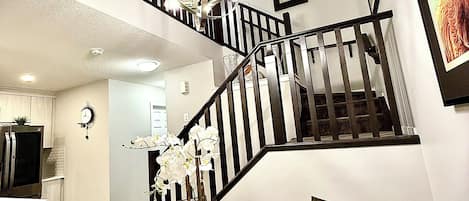 A dining area with a round table set for four, a chandelier, and a staircase leading to an upper level.