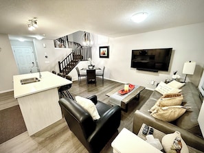 A modern living room with a sofa, a coffee table, a TV, and a staircase leading to another level. - Free Car garage|3BR|YYC|Banff|Canmore|Winsport|Stampede (Calgary)