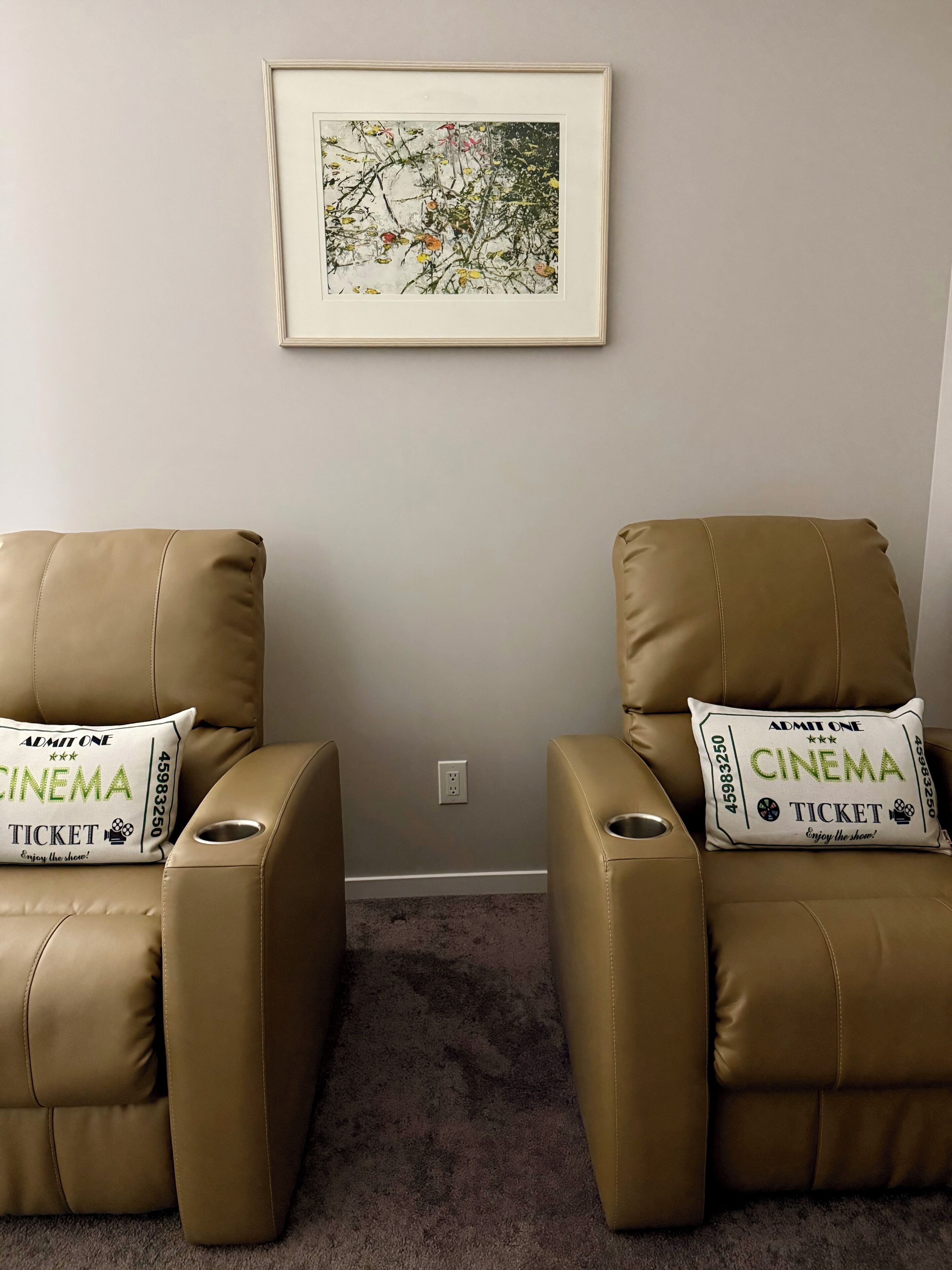 A room with two reclining chairs, each with a pillow featuring cinema ticket text.