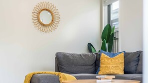 Un salon avec un canapé gris, une table basse ronde, un plaid jaune et un grand miroir doté d’un cadre en forme de soleil.