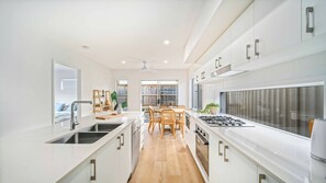 A modern kitchen with white cabinetry, a central island, and a dining area with a table and chairs. - Tuckeroo Retreat -Peaceful home in Mullumbimby - views of Mt Chincogan (Mullumbimby)