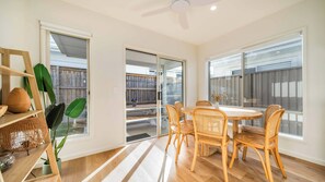 A dining area with a round table and wicker chairs, large windows, and a ceiling fan. - Tuckeroo Retreat -Peaceful home in Mullumbimby - views of Mt Chincogan (Mullumbimby)