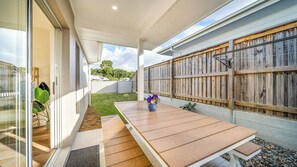 A covered patio with a wooden table and a flower pot, a grassy yard, and a wooden fence. - Tuckeroo Retreat -Peaceful home in Mullumbimby - views of Mt Chincogan (Mullumbimby)