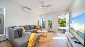 A modern living room with a grey sectional sofa, a round coffee table, and a large flat-screen TV. - Tuckeroo Retreat -Peaceful home in Mullumbimby - views of Mt Chincogan (Mullumbimby)