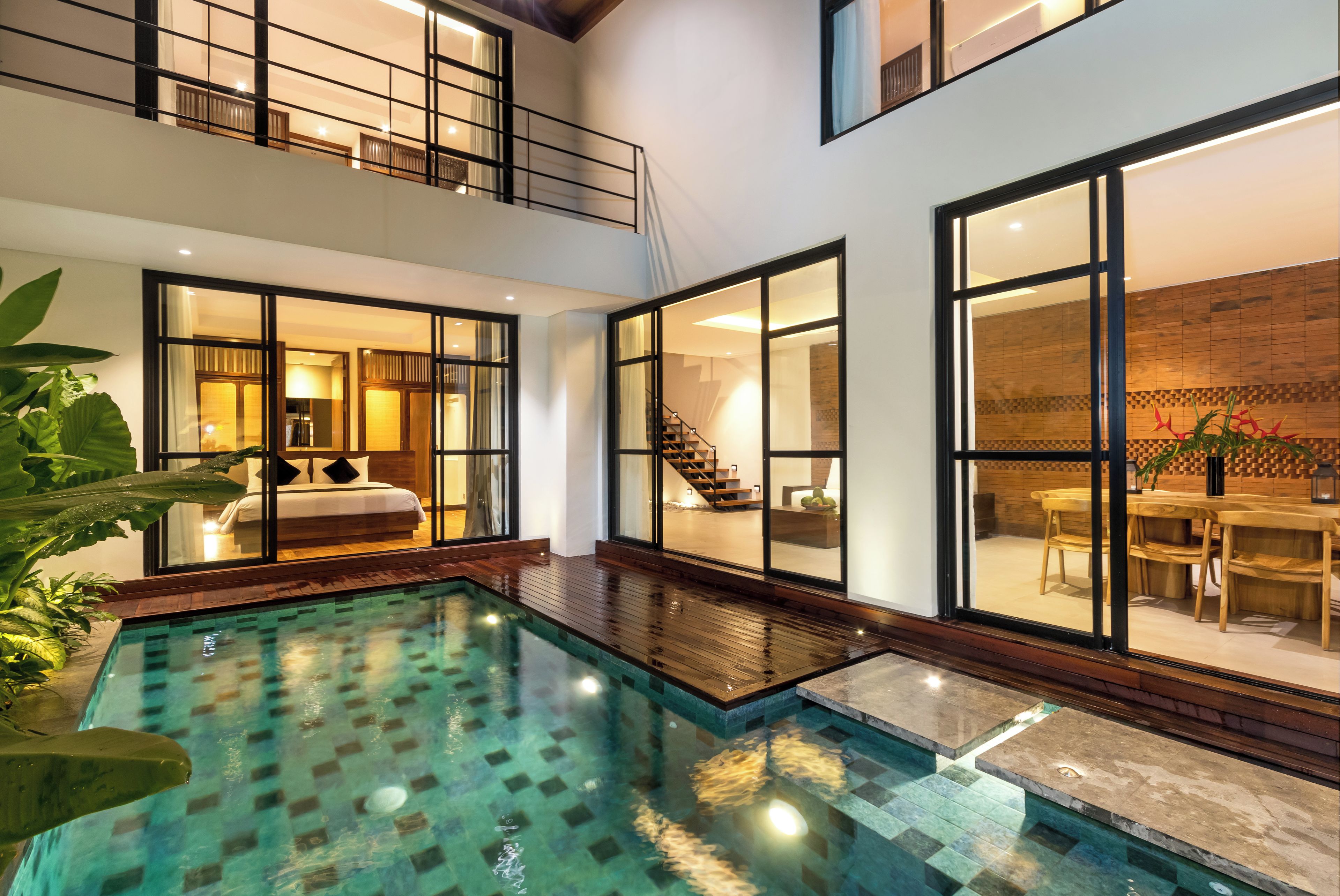 A modern interior with a central swimming pool, wooden flooring, and large glass doors leading to bedrooms and a dining area.