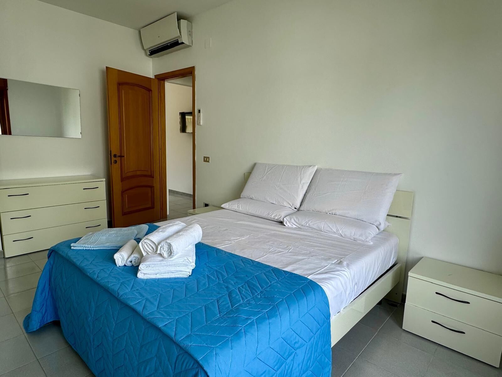 Une chambre d’hôtel comprenant un lit, une table de chevet, une commode et une porte donnant sur une autre pièce.