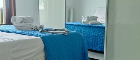 A hotel room with two beds, one with a blue quilt and the other with white bedding. There are folded towels on each bed.