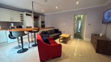 A modern living room with a red sofa, a wooden coffee table, and a kitchen area with a dining table and chairs.