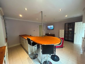 A modern kitchen with a central island, a dining area with a round table and chairs, a television mounted on the wall, and a door leading to another room.