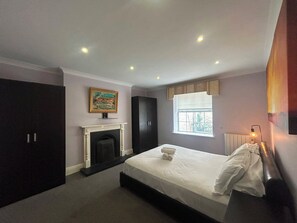 A bedroom with a bed, a fireplace, a window, and a painting on the wall.