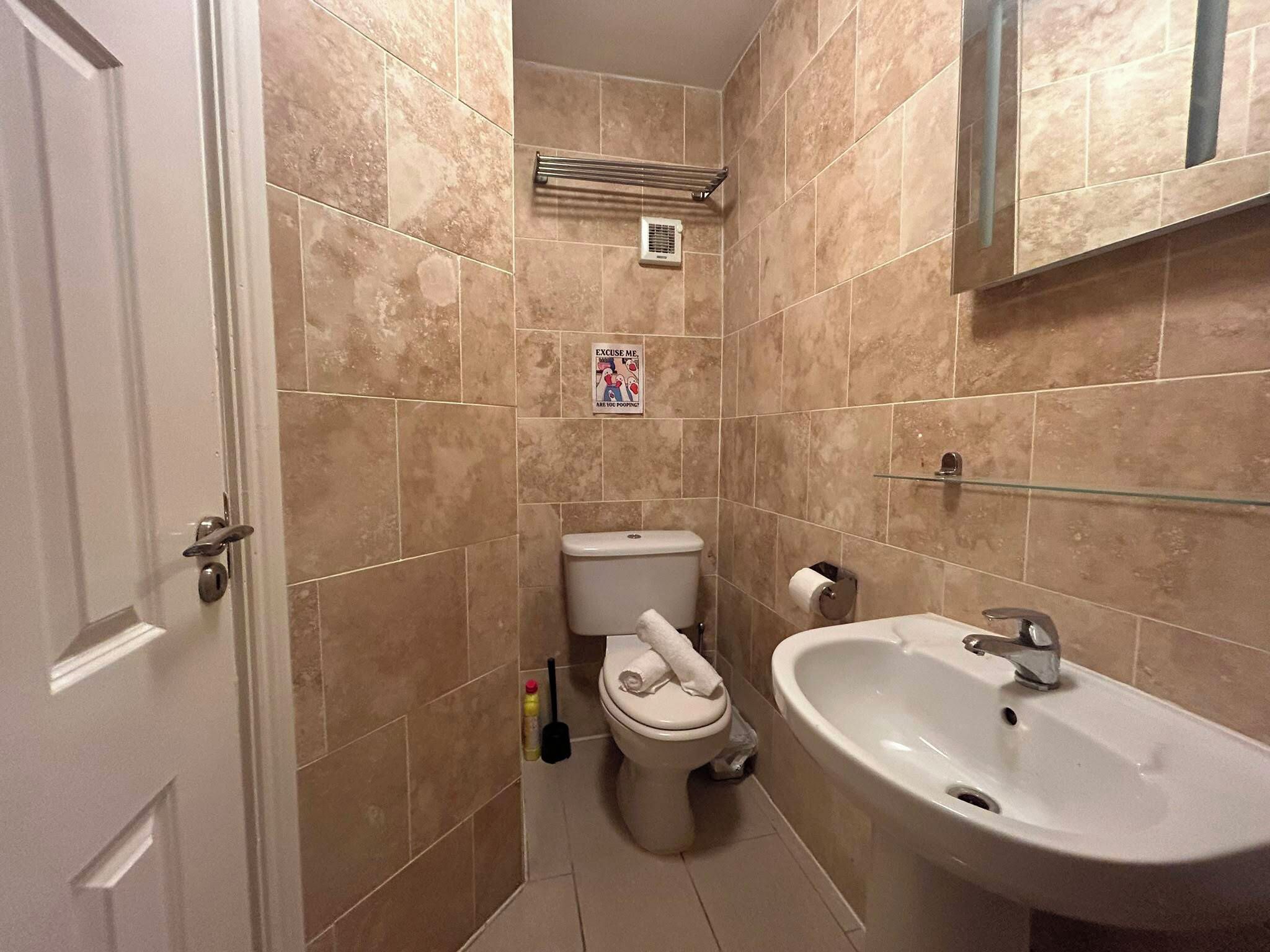 A bathroom with beige tiles, a toilet, a sink, a towel, and a hand dryer.