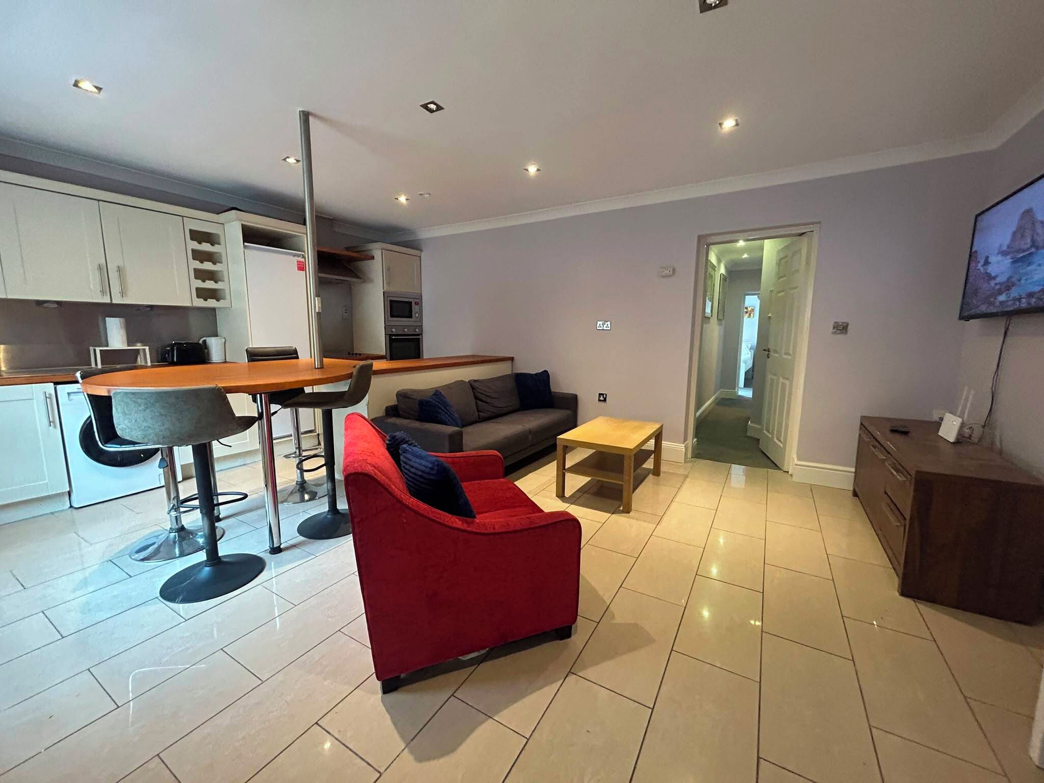 A modern living room with a red sofa, a wooden coffee table, and a kitchen area with a dining table and chairs.