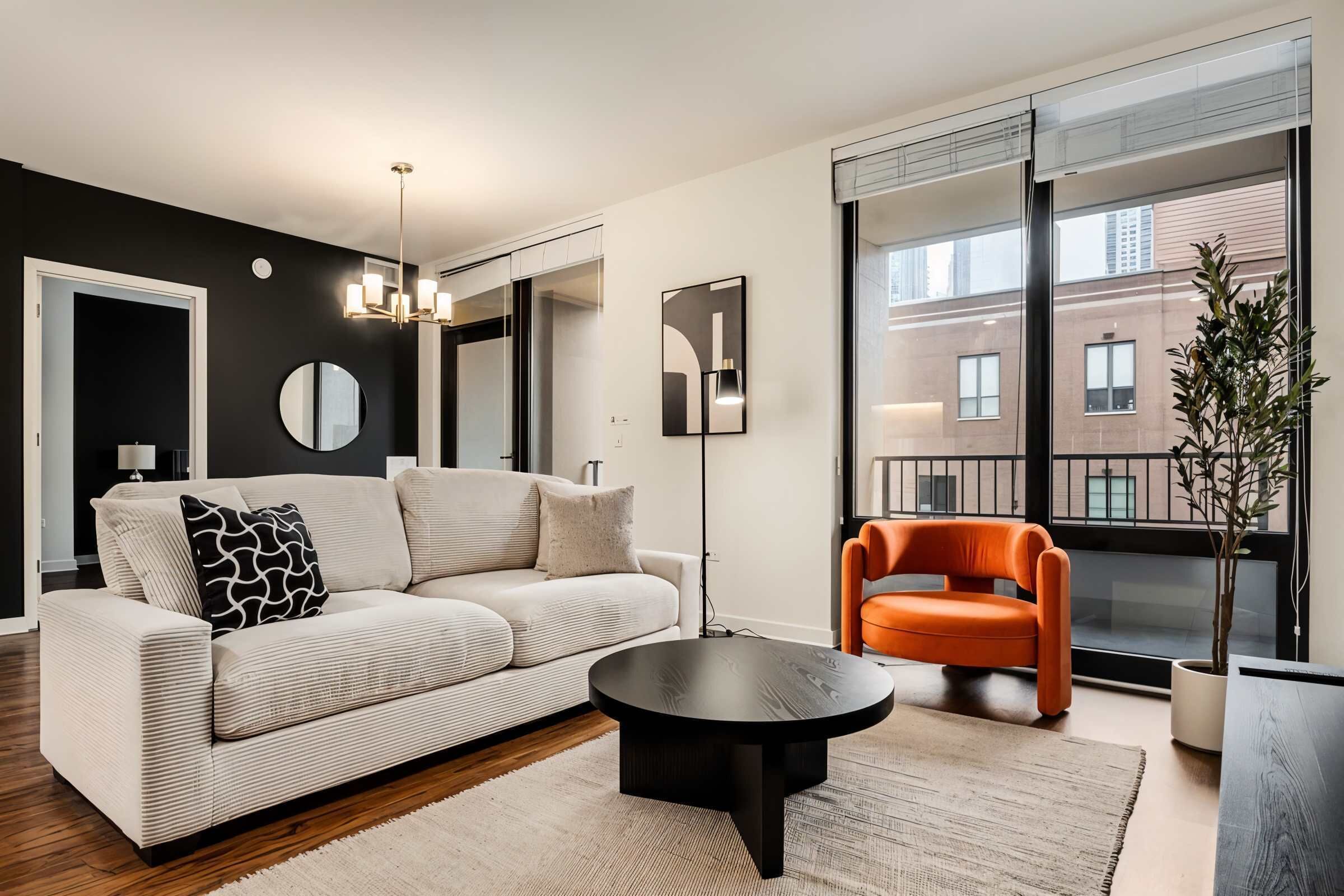 A modern living room with a sofa, a round coffee table, and a chair. There is a large mirror on the wall and a potted plant.